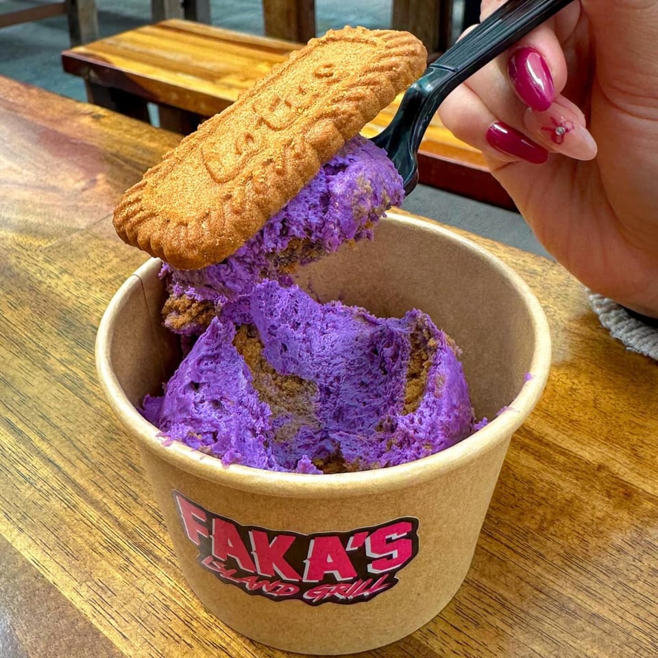 Purple ube ice cream with cookie crumbles in a Faka's Land and Grill cup, topped with a large cookie.