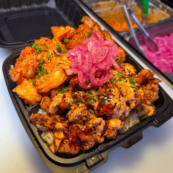 A takeout container filled with rice, fried chicken, shrimp, sauces, and pickled red onions.