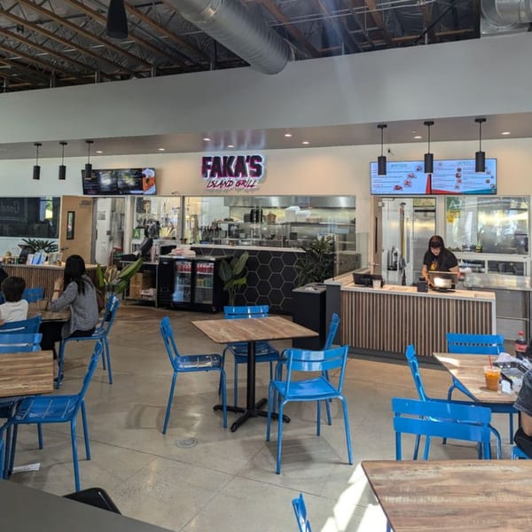 Faka's Island Grill restaurant interior with blue chairs, wooden tables, and a server behind the counter.