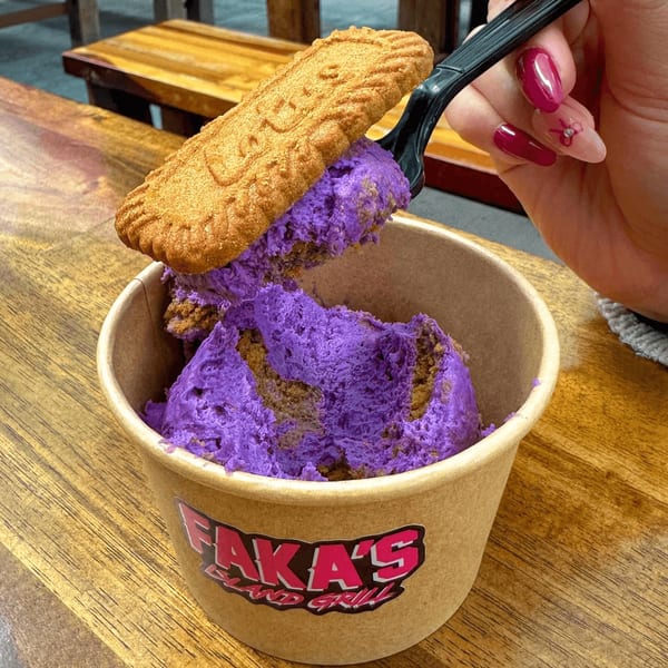 A hand holding a spoon with purple ice cream and a cookie over a cup of ice cream.