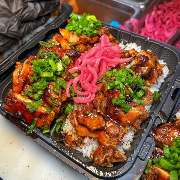 Teriyaki chicken and rice topped with bright pink pickled onions and green scallions in a black container.