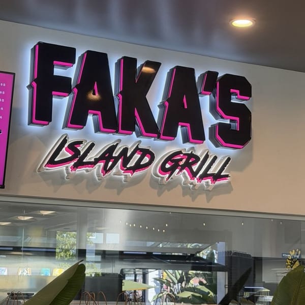 Faka's Island Grill restaurant sign with black and pink lettering, illuminated by white backlighting.