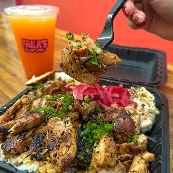 A hand holds a forkful of grilled chicken over a takeout container with rice, pickled onions, and macaroni salad, with a Faka's drink.