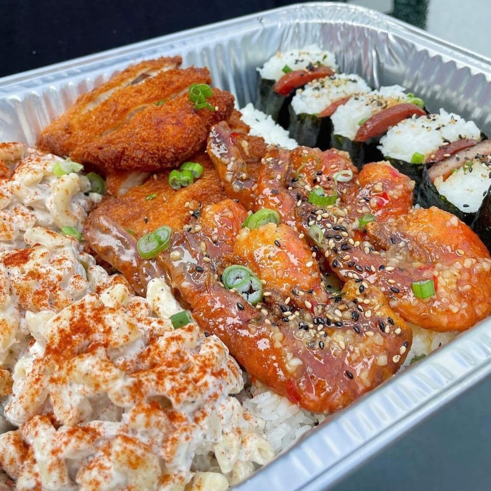 A takeout tray with crispy fried chicken, glazed chicken, macaroni salad, and spam musubi.