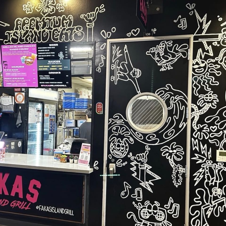 A restaurant counter with a menu board and a black wall with white cartoon-style drawings.