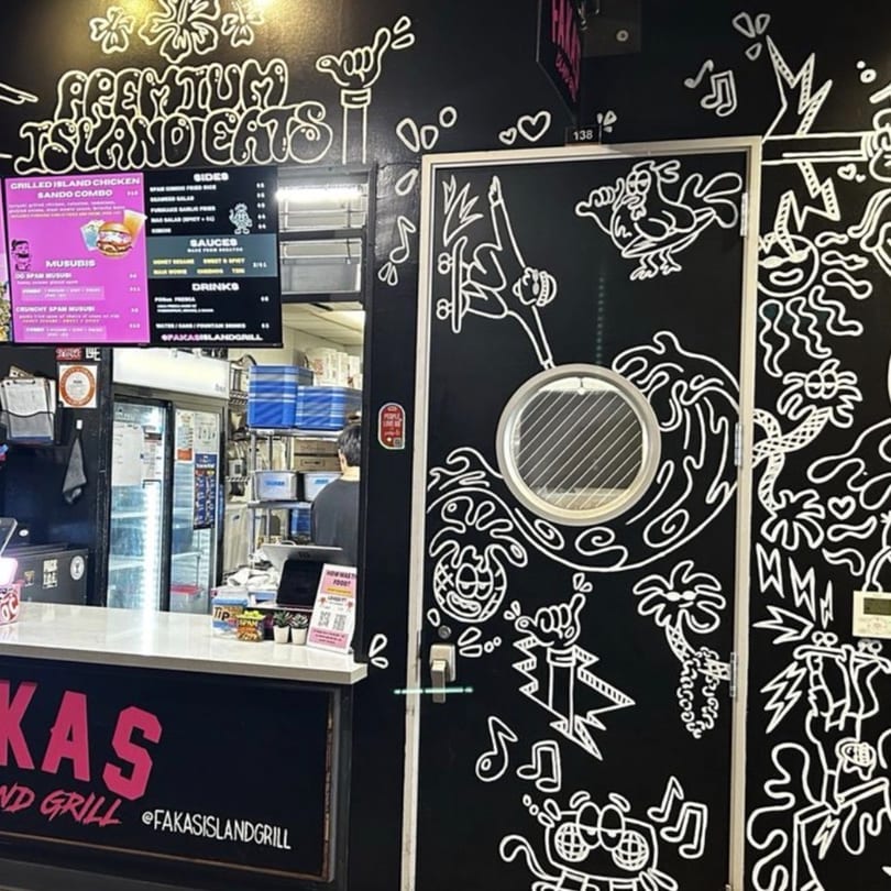 A restaurant counter with a menu board and a black wall with white cartoon-style drawings.