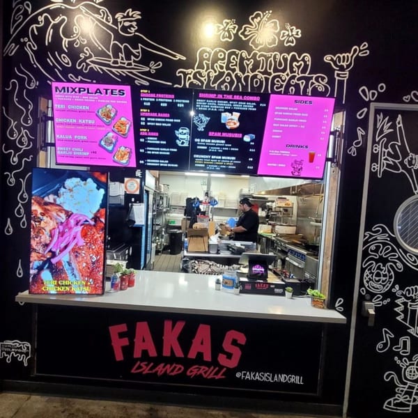 A restaurant counter with digital menus, a food display, and a chef working in the kitchen.