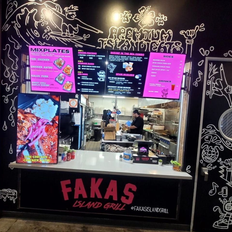 A restaurant counter with digital menus, a food display, and a chef working in the kitchen.