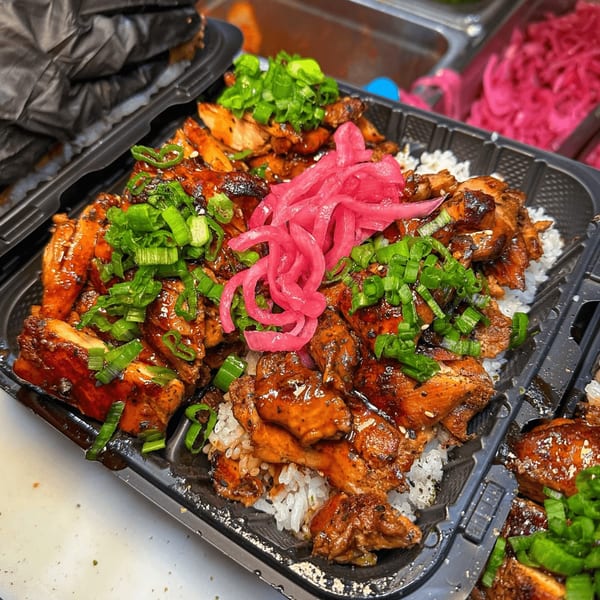 Teriyaki chicken with rice, topped with green onions and pickled red onions in a black container.