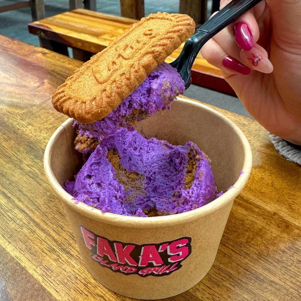 A hand holding a spoon with purple ice cream and a cookie, scooping from a Faka's cup.