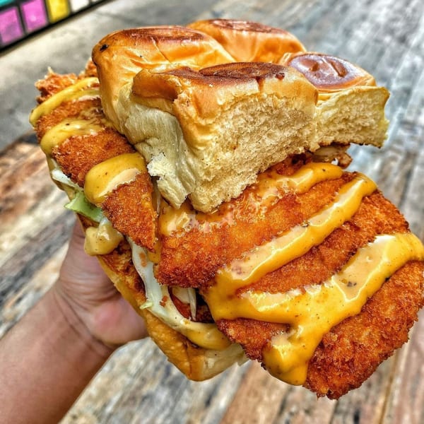 Hand holding a large fried chicken sandwich with sauce and lettuce on a brioche bun.