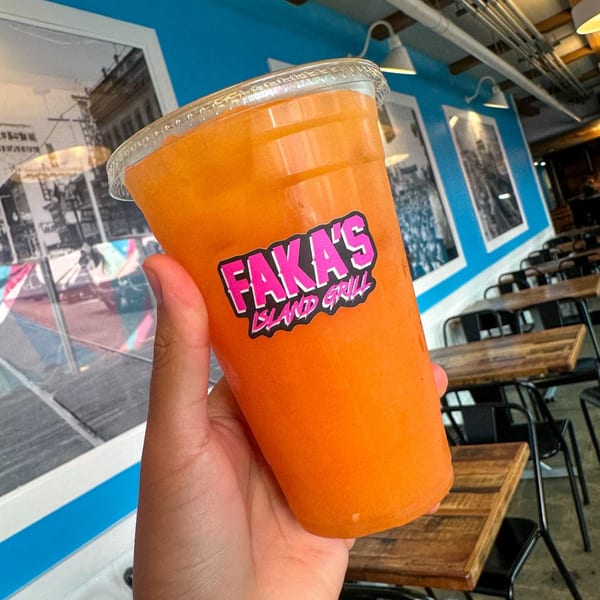 Hand holding a Faka's Island Grill branded orange drink inside the restaurant.